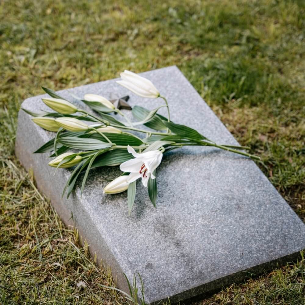 Sängerin für die Beerdigung im Freien. Auf dem Bild liegen weiße Blumen auf einem Grabstein im Freien.