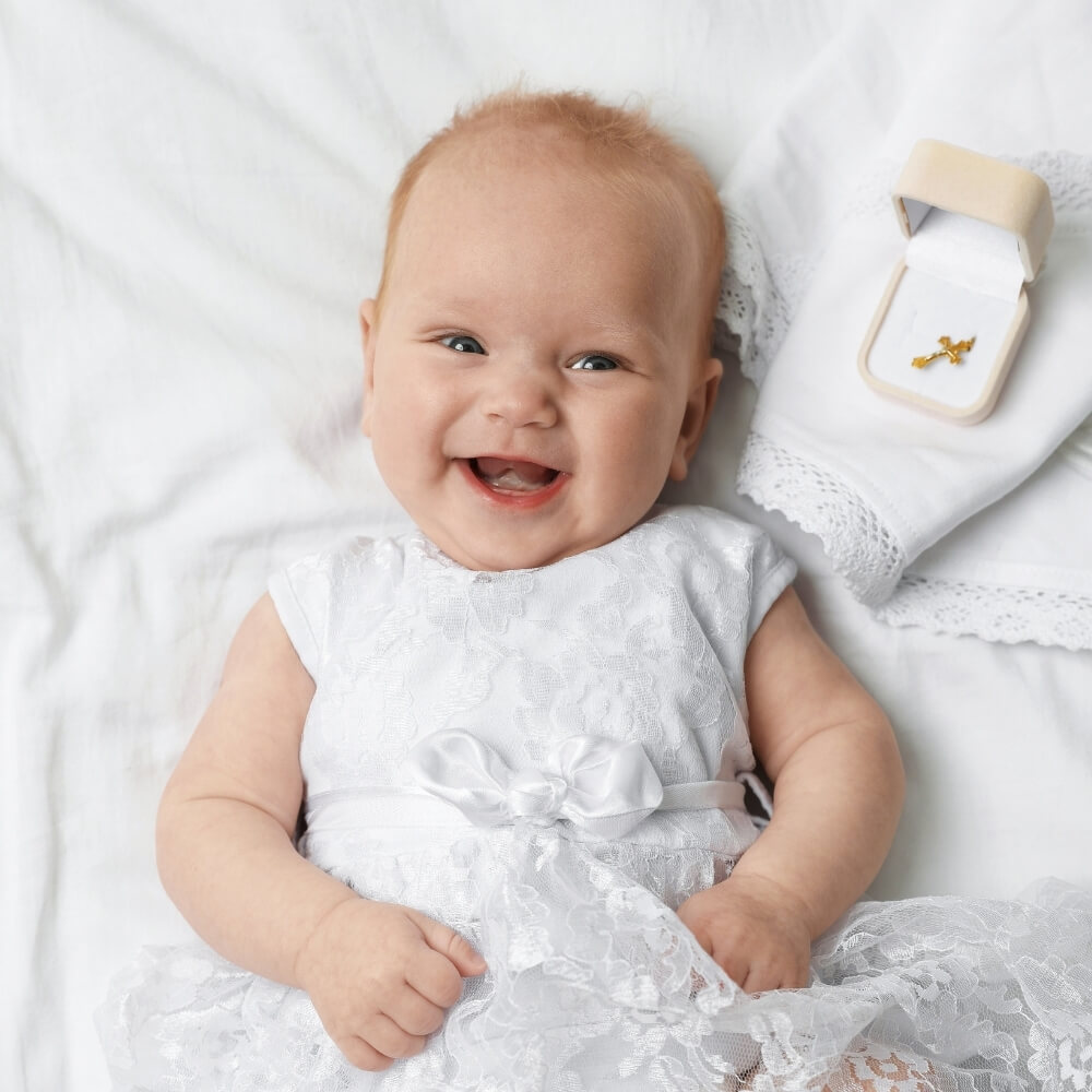 Sängerin zur Taufe. Ein Baby in einem weißen Kleid für die Taufe lächelt glücklich in die Kamera.